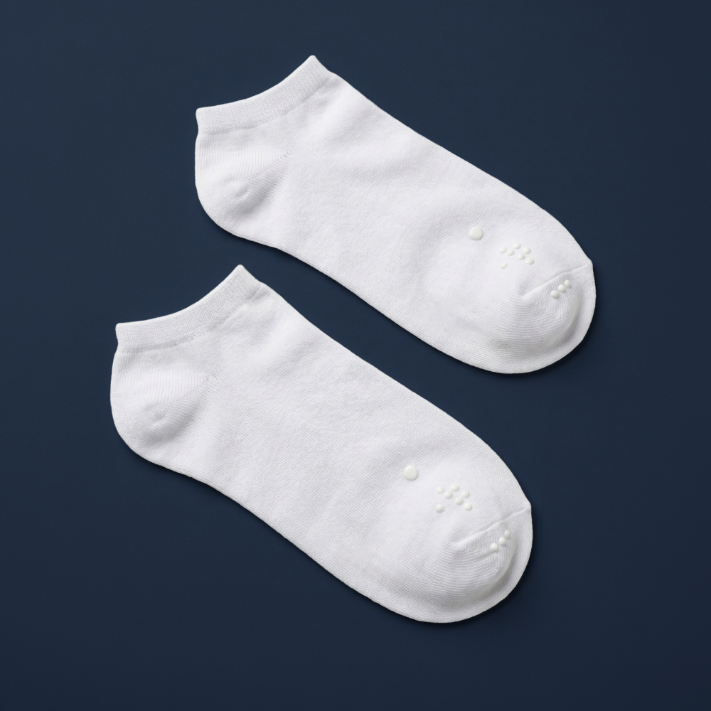 A pair of Matchables white ankle socks with white tactile markers, laid flat against a high-contrast dark navy background.