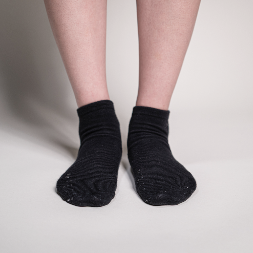 Front view of a person wearing black ankle socks on a light background, emphasizing the placement of the identification markers on the toes.