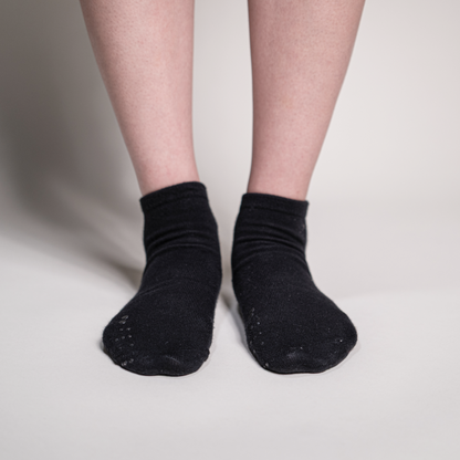 Front view of a person wearing black ankle socks on a light background, emphasizing the placement of the identification markers on the toes.