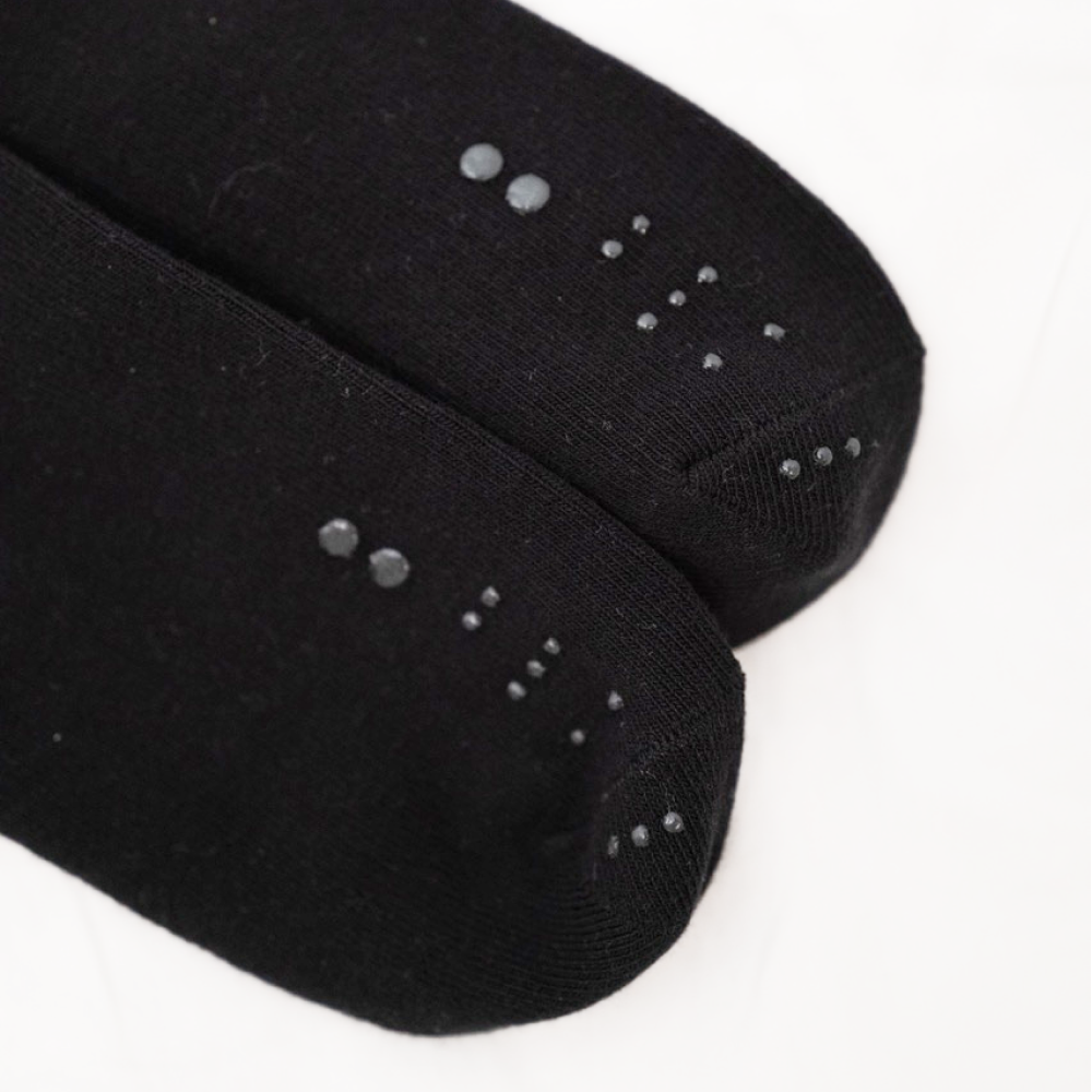 Close-up of the toe section of two black socks, highlighting the printed black tactile dots that form the specific pattern for the color Black.